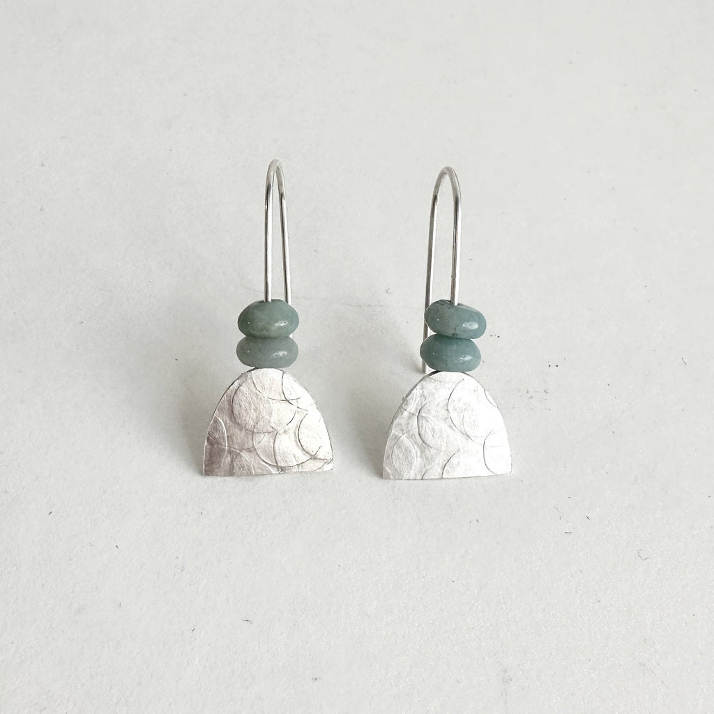 Textured silver half oval dangle earrings with two muted green beads, arched earring wire. Held in place with clear plastic backings. www.wyckoffsmith.com