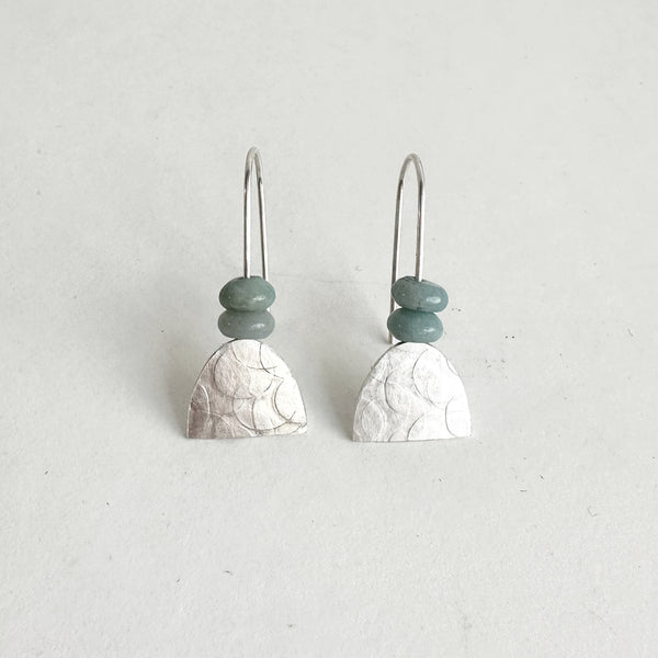 Textured silver half oval dangle earrings with two muted green beads, arched earring wire. Held in place with clear plastic backings. www.wyckoffsmith.com