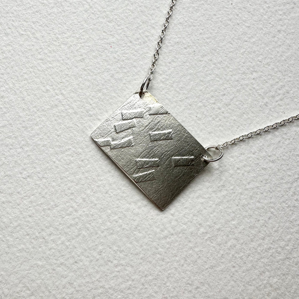 Diagonal photograph of rectangular silver pendant with dash texture on an adjustable chain - www.wyckoffsmith.com - Michele Wyckoff Smith