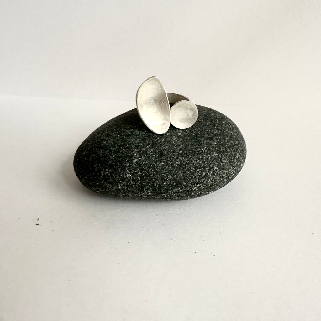 Open ring with a graphic shaped oval and a circle, textured ring shank sitting on a dark stone. www.wyckoffsmith.com