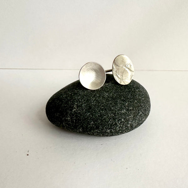 Side by side open silver ring - circle and textured oval shapes sitting on a dark pebble. www.wyckoffsmith.com