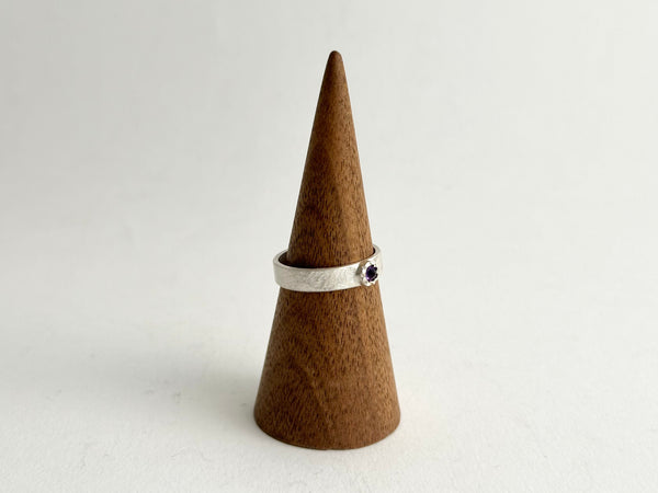 Side view of Tudor set inverted amethyst on a silver rough hammered band shown on wooden cone - www.wyckoffsmith.com