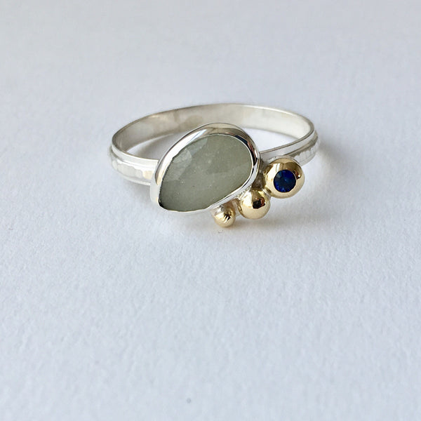 Larger grey faceted oval sapphire with 3 gold balls along side. There is a blue sapphire set in the largest 18 ct gold ball.