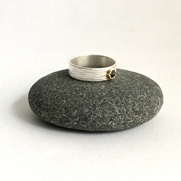 Side view of rose cut cognac diamond in 18 ct hammer set bezel on a wide textured silver band on top of a pebble - www.wyckoffsmith.com