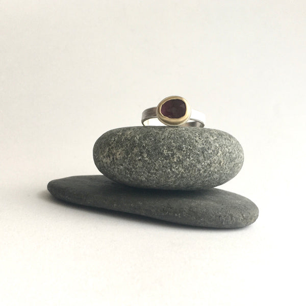 Front view of pink rose cut tourmaline set in 18 ct gold on a textured silver band on top of two pebbles on www.wyckoffsmith.com silver and gold jewelry