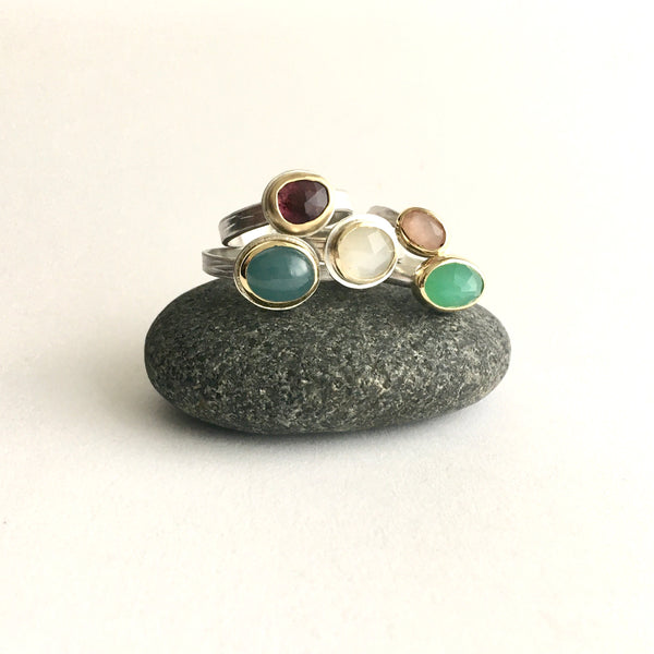 Collection of stacking gemstone rings on top of a pebble on www.wyckoffsmith.com left to right: aquamarine, pink tourmaline, whilte moonstone, peach moonstone and chrysoprase