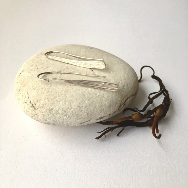 Silver seaweed dangle earrings on white pebble and seaweed beside it. www.wyckoffsmith.com