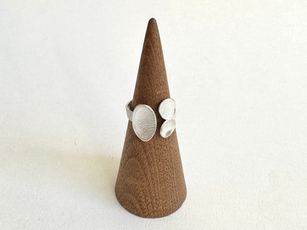 Textured oval and two small pebble shapes on an adjustable ring shown on a wooden ring holder - www.wyckoffsmith.com