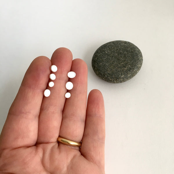 Assorted single stud earrings held between fingers with pebble in the background - www.wyckoffsmith.com