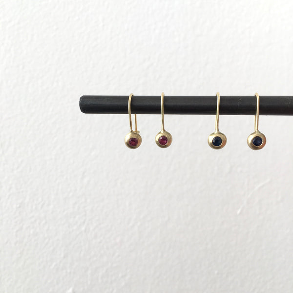 Ruby and 18 ct gold earrings on the left, sapphire and 18 ct gold earrings on the right hanging from a steel bar - www.wyckoffsmith.com - recycled gold earrings