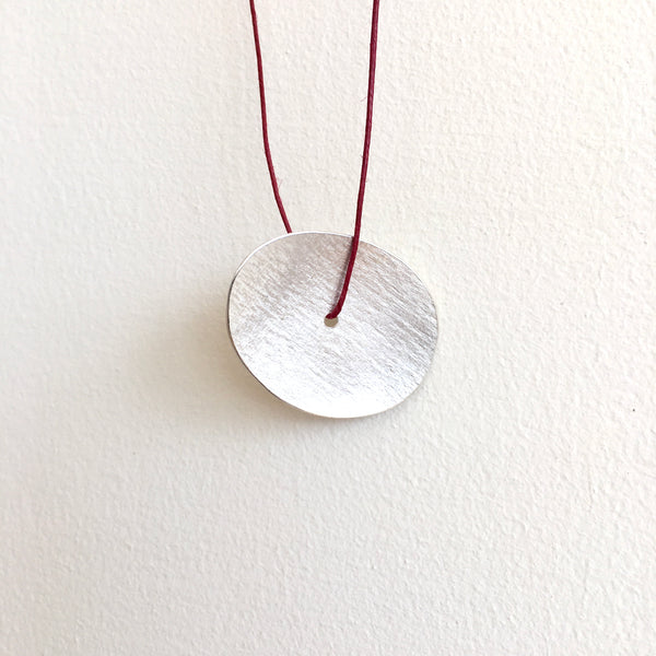Lightly textured oval pendant on red thread with centre hole - www.wyckoffsmith.com