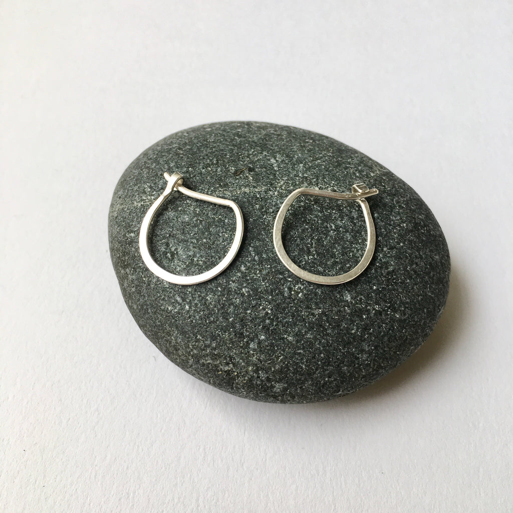 Hand forged silver hoop earrings with a U shape sitting on a pebble - Wyckoff Smith Jewellery