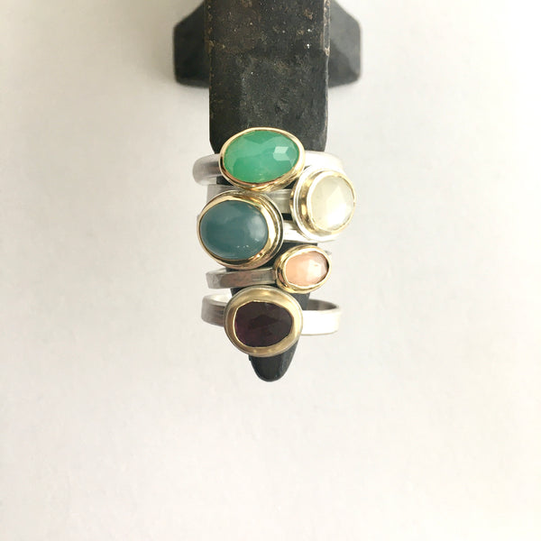 Collection of gemstone stacking rings on a miniature jewellers anvil on by Michele Wyckoff Smith on www.wyckoffsmith.com top to bottom: chrysoprase, white moonstone, aquamarine, peach moonstone and pink tourmaline set in 18 ct gold on silver bands
