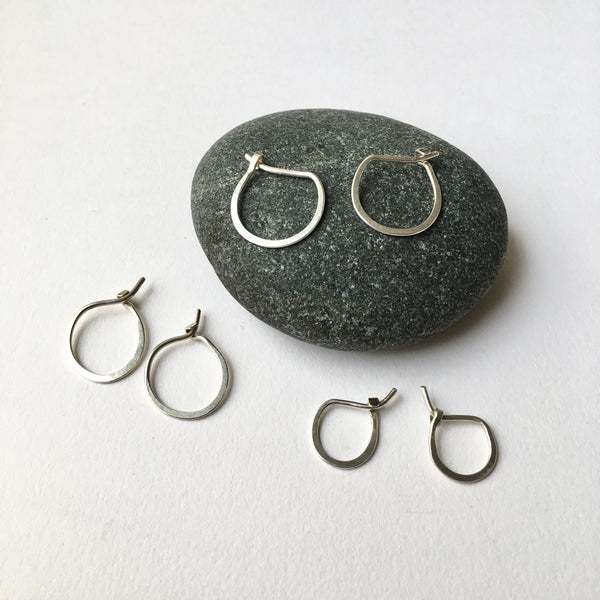 Assortment of hand forged silver hoop earrings sitting on a pebble - Wyckoff Smith Jewellery
