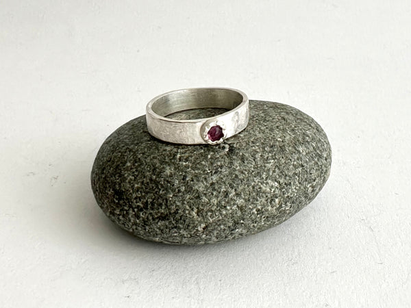 Inverted ruby with a Tudor setting on a silver band shown on a pebble - www.wyckoffsmith.com