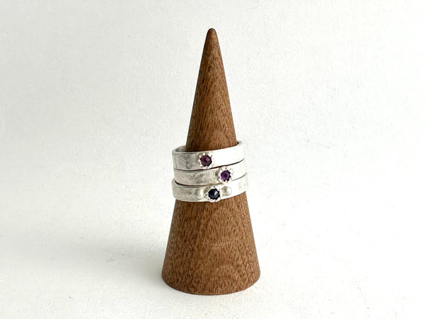 Stack of Tudor set ruby, amethyst and sapphires on silver rough hammered bands shown on wooden cone - www.wyckoffsmith.com