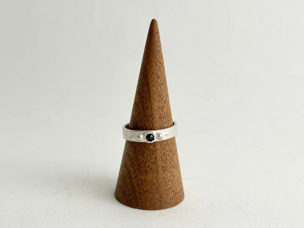 Front view of Tudor Set inverted sapphire on a wide hammered texture silver ring shown on a wooden cone - www.wyckoffsmith.com