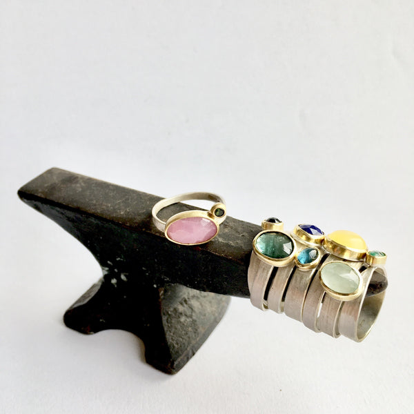 Assortment of brightly coloured gemstone rings set in 18 ct gold sitting on a miniature anvil by Michele Wyckoff Smith