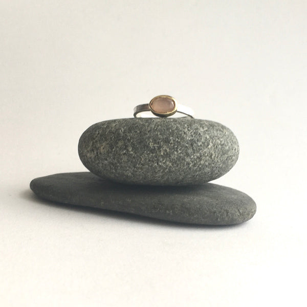 Peach moonstone set in gold on silver band on top of two pebbles by Michele Wyckoff Smith