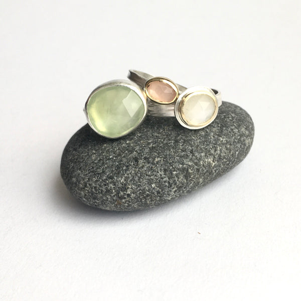 Collection of stacking gemstone rings on top of a pebble on www.wyckoffsmith.com left to right: prehnite, peach moonstone and white moonstone