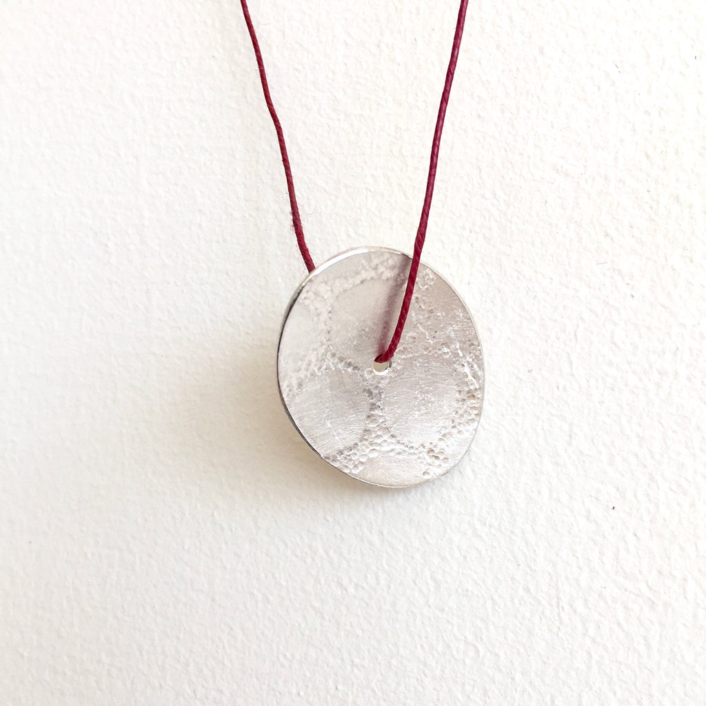 Oval pendant with circle mark texture on red thread - www.wyckoffsmith.com