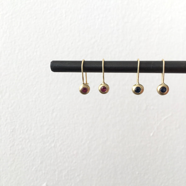 Ruby and 18 ct gold earrings on the left, sapphire and 18 ct gold earrings on the right hanging from a steel bar - www.wyckoffsmith.com - recycled gold earrings 
